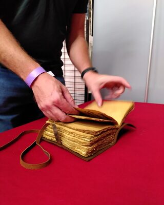 Des mains tournent les pages d’un vieux livre sur la table du stand.