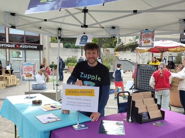 L’animateur, souriant, accoudé à la table du stand.