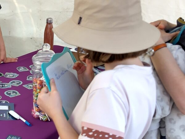 Une enfant, de dos, écrit sa réponse sur une ardoise devant la table du stand.